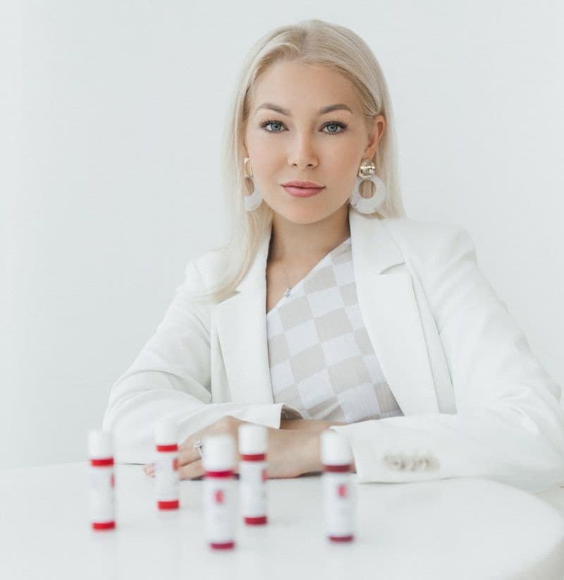 Vasilisa Klamka in a white jacket, sitting at a table with bottles of lip pigment